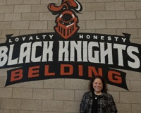 Photo of Woman in front of Belding Black Knights Logo