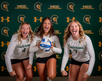 Three MCC volleyball players yell toward the camera to display enthusiasm. The middle player is holding a volleyball.