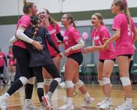 Six MCC volleyball players, wearing their pink jerseys, smile and celebrate together during a game.