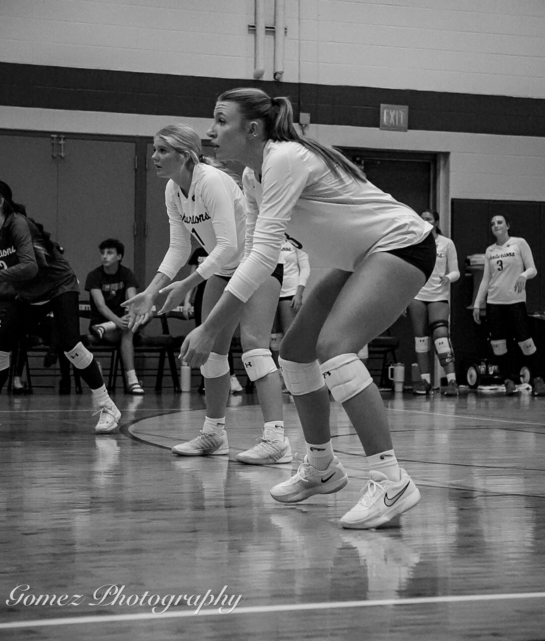 Black and white photo of two MCC volleyball players squatting down and preparing to hit the ball coming over the net. 
