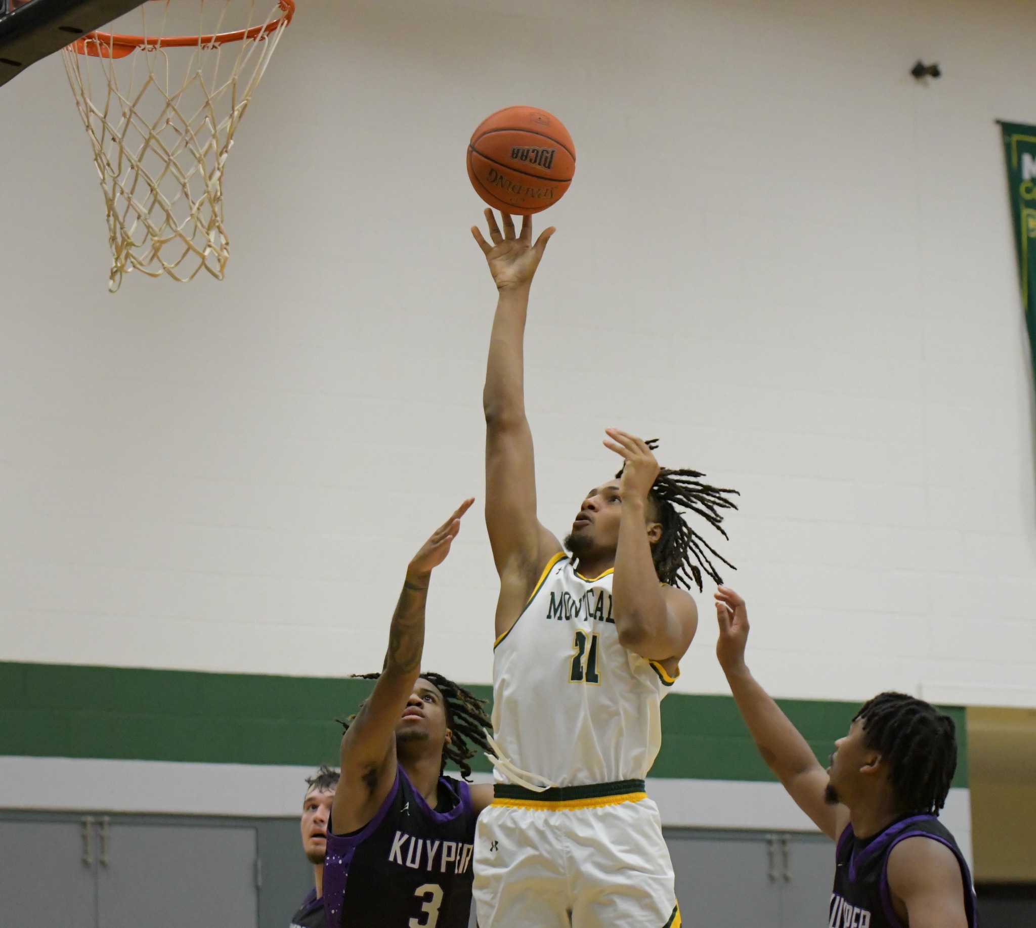MCC Men's Basketball player jumps to take a shot while two opposing players attemot to block/catch the rebound. 