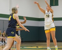 MCC basketball player Kennedy Schilling takes a three-point shot while being approached by two opposing players.