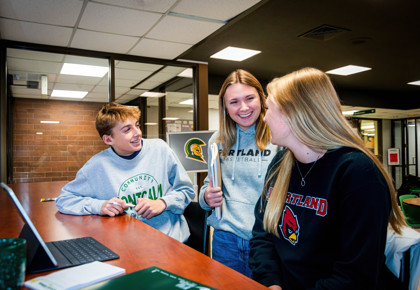 Three MCC students smiling while conversing in the Woodside Café.