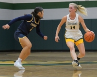 An MCC basketball player dribbles up the court with the ball in her left hand with a defender to her right.