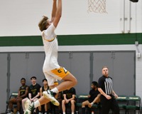 An MCC men's basketball player jumps and extends the ball above his head for a dunk attempt.