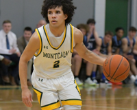 An MCC basketball player with the ball in his left hand dribbles up the court.