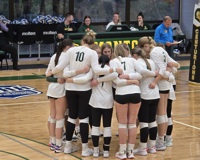 The MCC volleyball team huddles up in a circle on the court during a game.