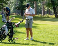 MCC men's golfer standing on the green grass next to his golf bag looking down at the score card.
